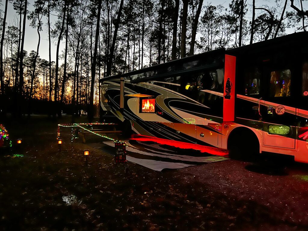 Large Class A motorhome parked at a wooded RV site at twilight in winter