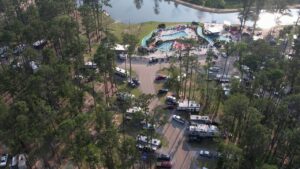 Aerial view of a Louisiana campground with RV sites among pines, pools, a lazy river, and a lake