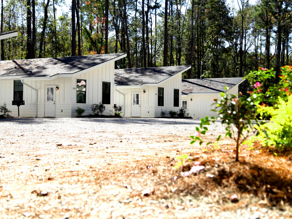 A row of modern white cabins with dark shingled roofs and black shutters at Fireside RV Resort, framed by tall pine trees