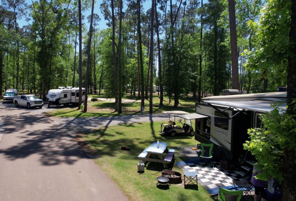 A fifth-wheel RV with an extended awning on a sunny wooded site at Fireside RV Resort in Ponchatoula, Louisiana.