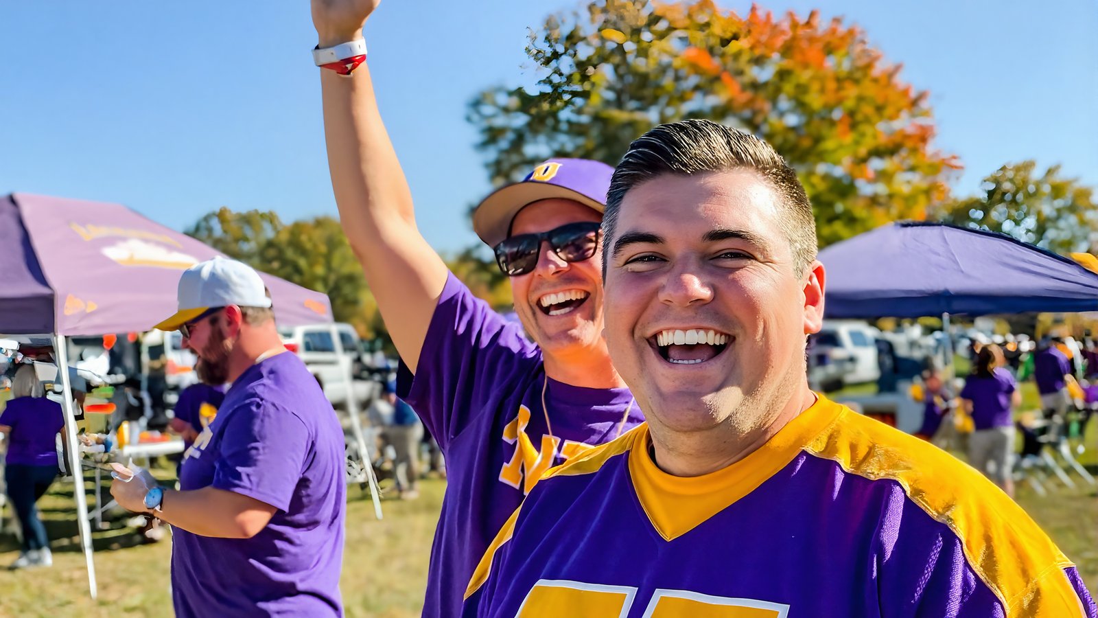 LSU fans in purple and gold cheering at a game-day tailgate