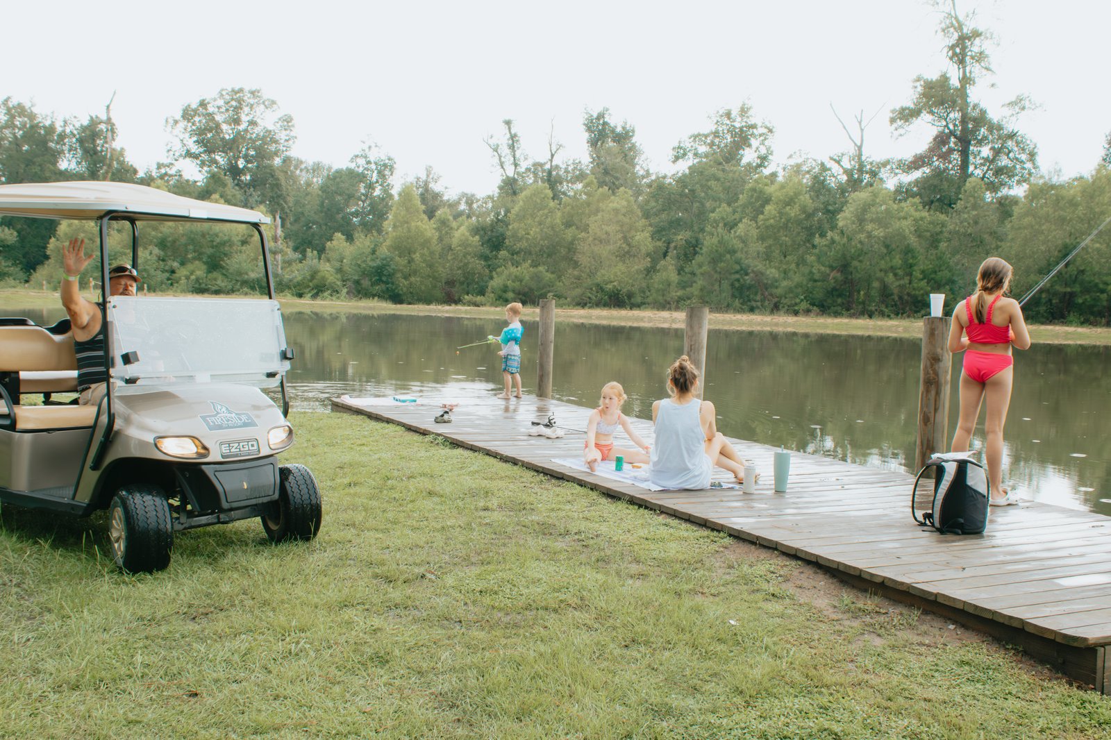 Family fishing and relaxing on the lakeside dock at Fireside RV Resort with a golf cart nearby
