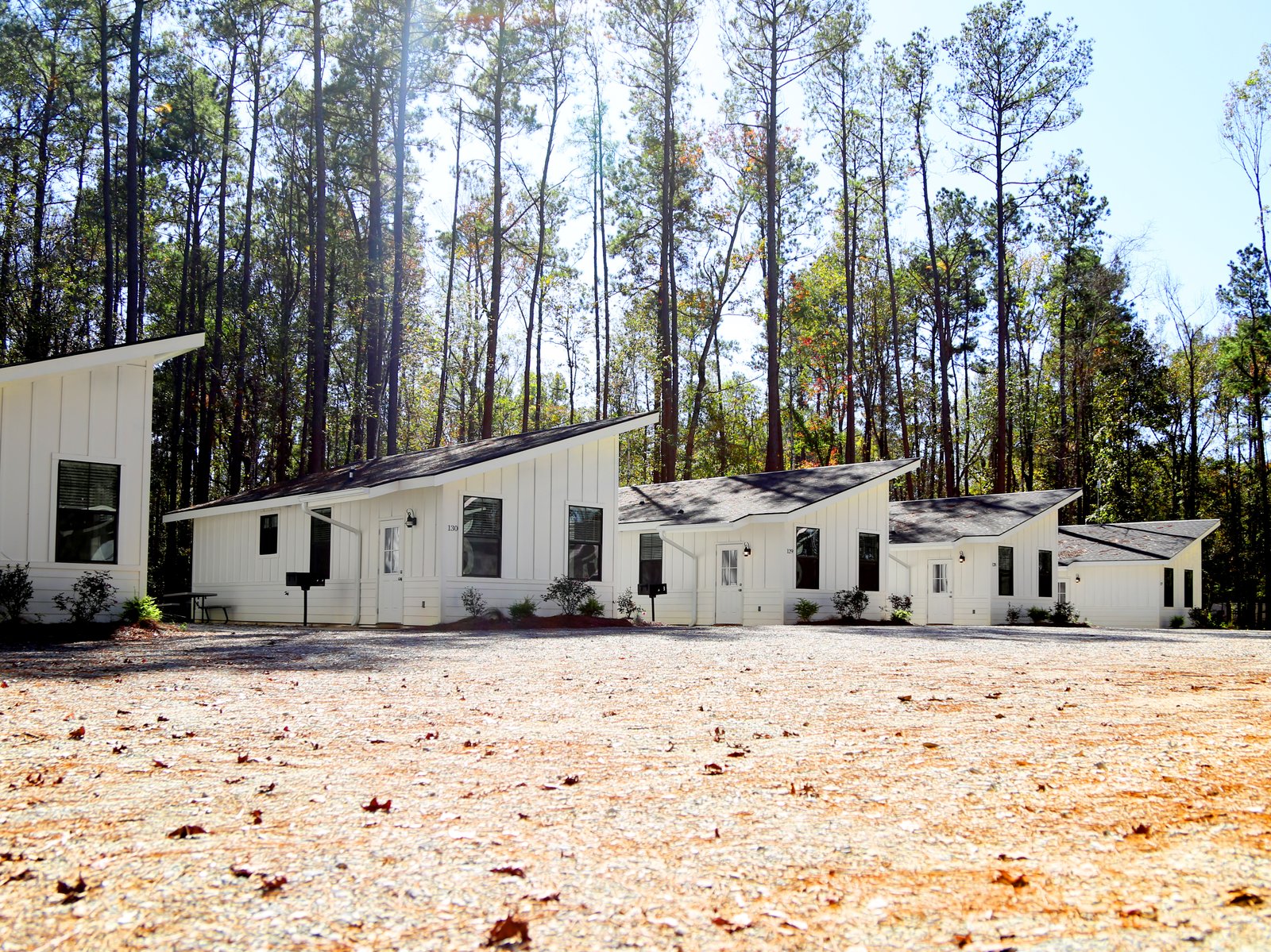 Row of modern white furnished cabins among tall pine trees at Fireside RV Resort in Ponchatoula