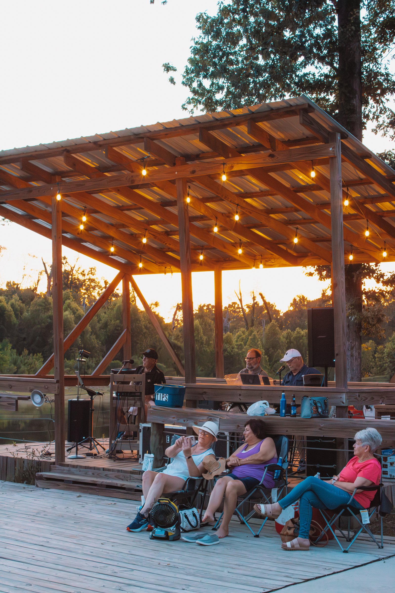 Guests relaxing under a string-lit lakeside pavilion at golden hour at Fireside RV Resort