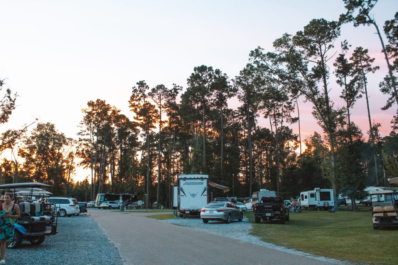 Full-hookup RV sites with rigs and golf carts along a gravel road at dusk at Fireside RV Resort near Slidell