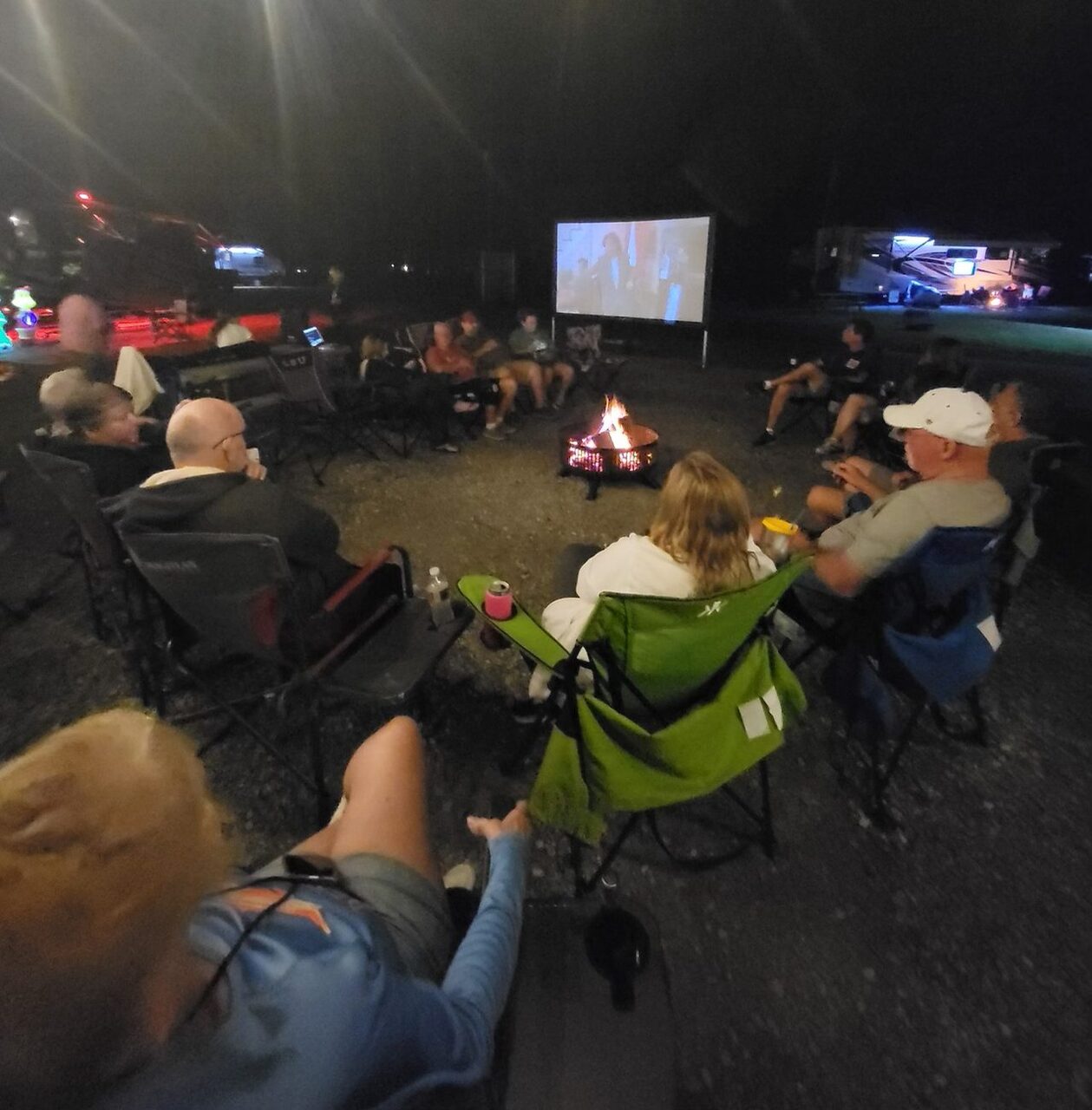 Guests gathered around a fire pit at night for an outdoor movie while camping near New Orleans