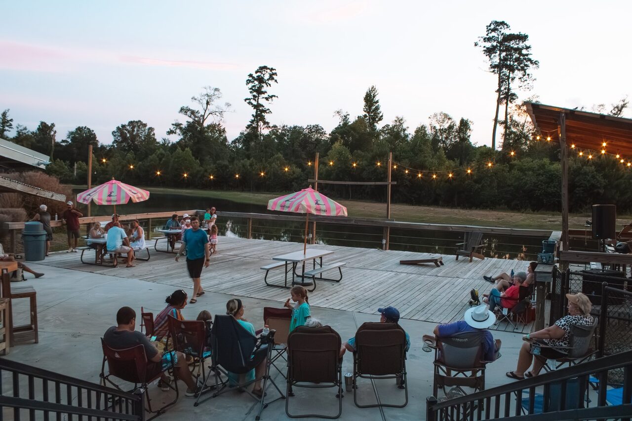 Guests relaxing on a lakeside deck under string lights at Fireside RV Resort in Ponchatoula