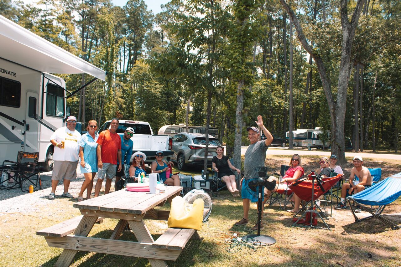 A group gathered for a cookout at a wooded full-hookup RV site at Fireside
