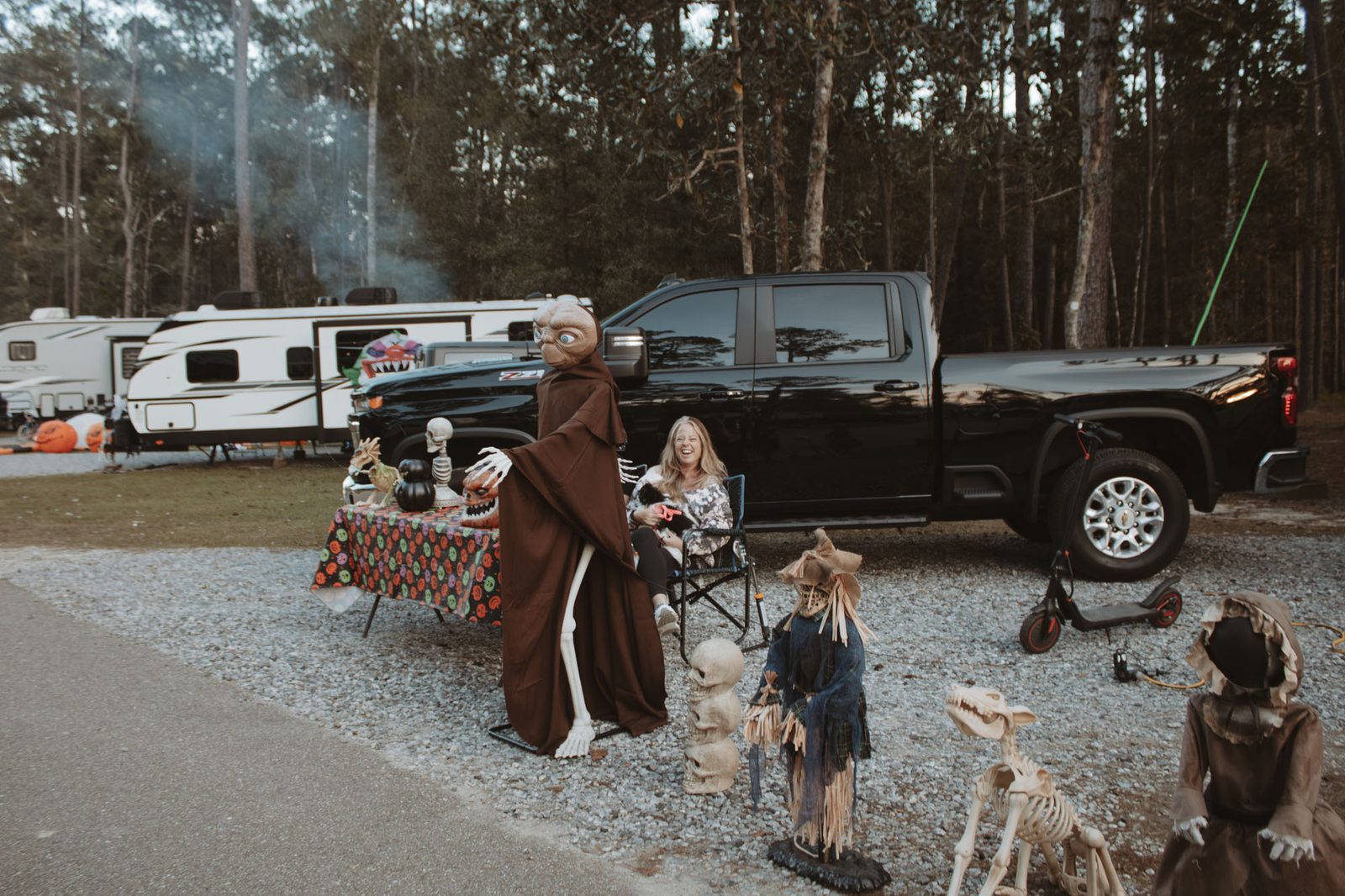 Guest laughing in a camp chair beside a black pickup truck at a Halloween-decorated RV site at Fireside RV Resort