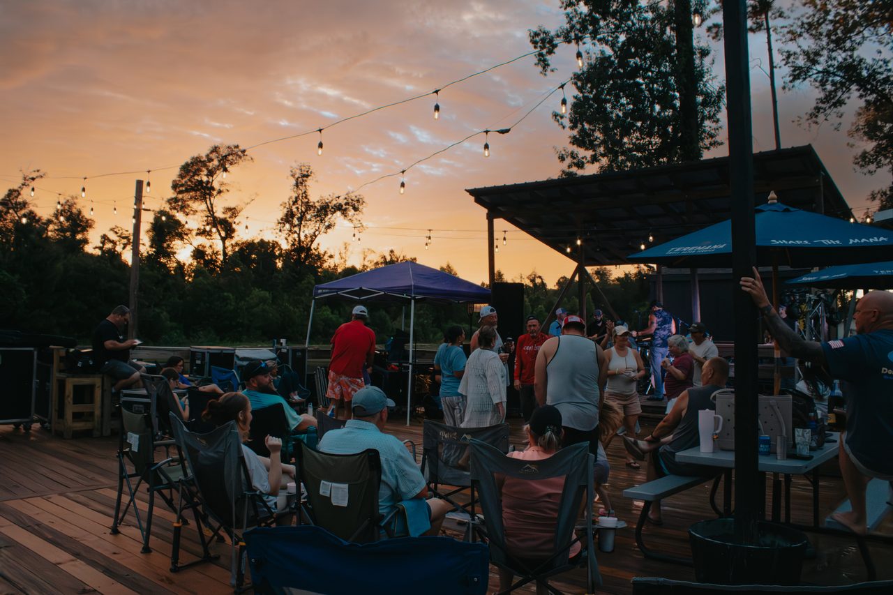 Campers relaxing in chairs at golden hour during a live music evening at an RV resort near New Orleans