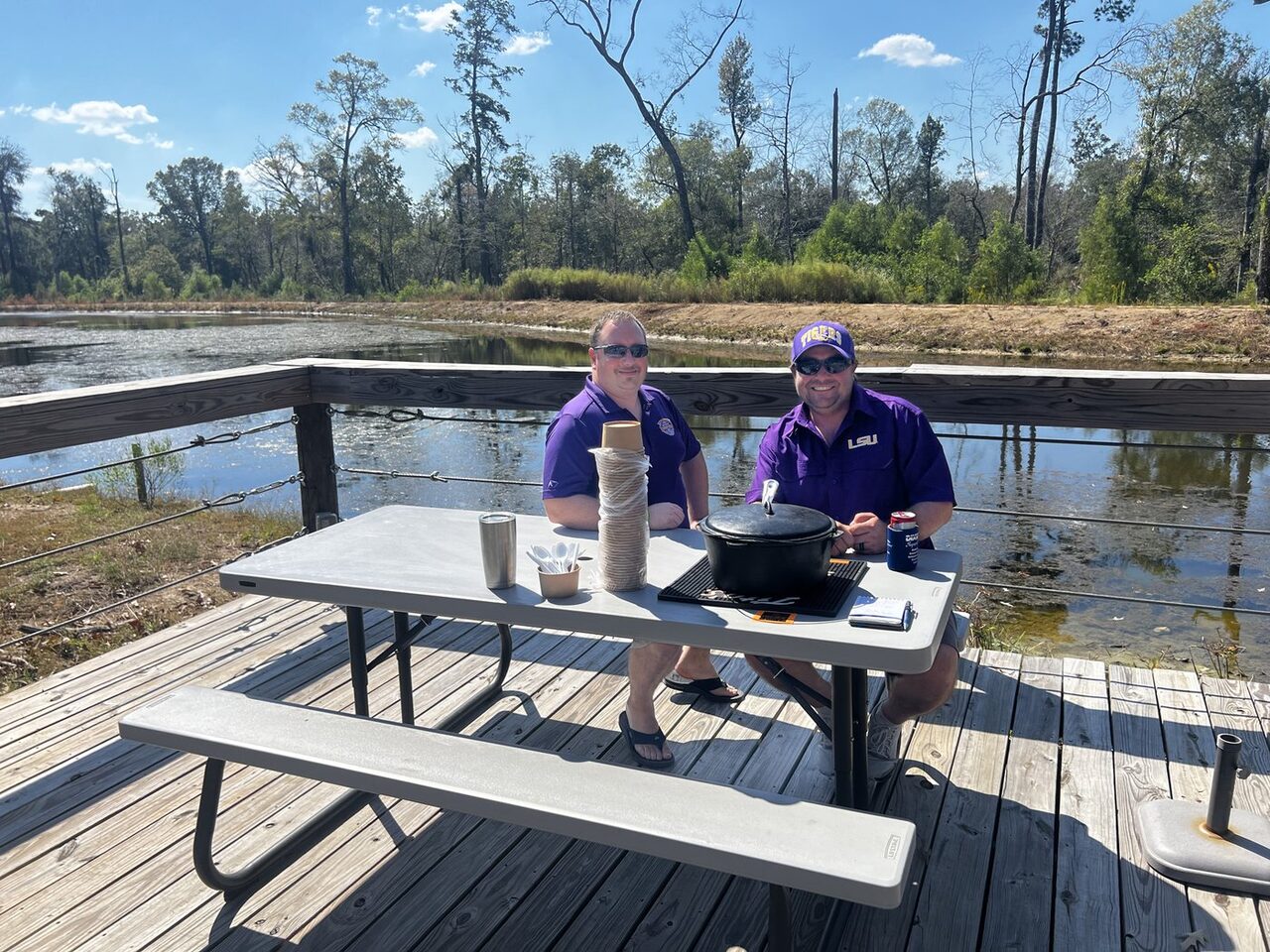 Two guests in LSU purple cooking on a deck over the pond at an RV park near Ponchatoula, Louisiana