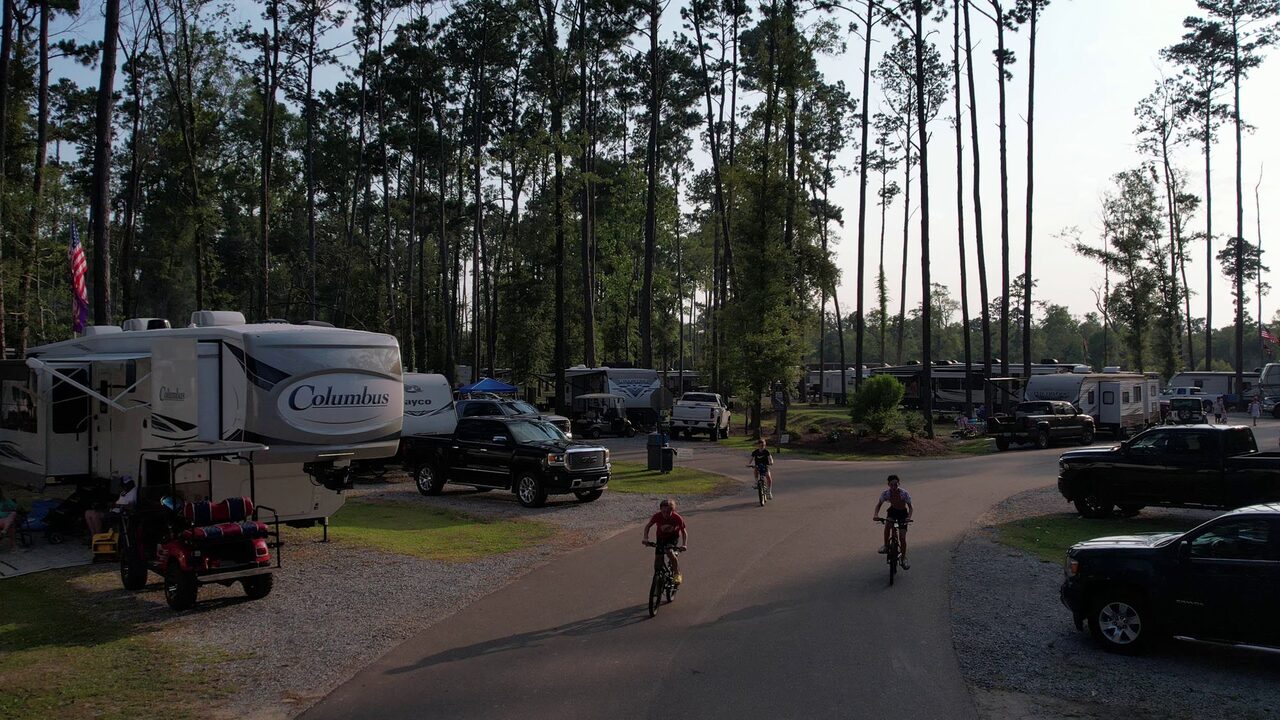 Paved interior road lined with RVs at a luxury RV park in Louisiana as kids ride bikes past