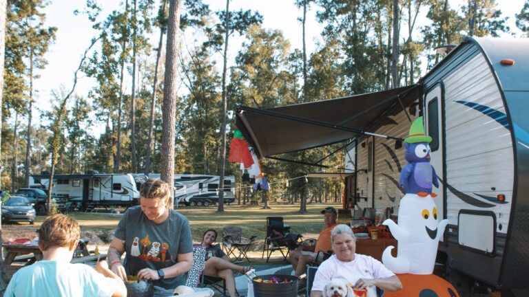 Family gathered around a fire ring beside their travel trailer at a luxury RV resort in Louisiana