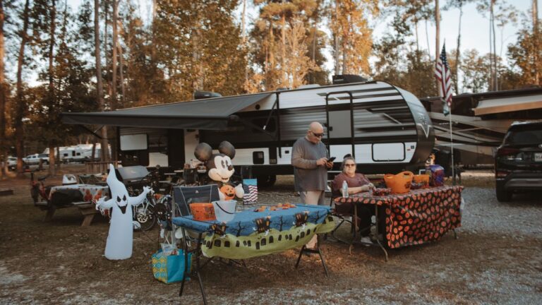 Couple at their Halloween-decorated travel trailer site at Fireside RV Resort near New Orleans in golden fall light