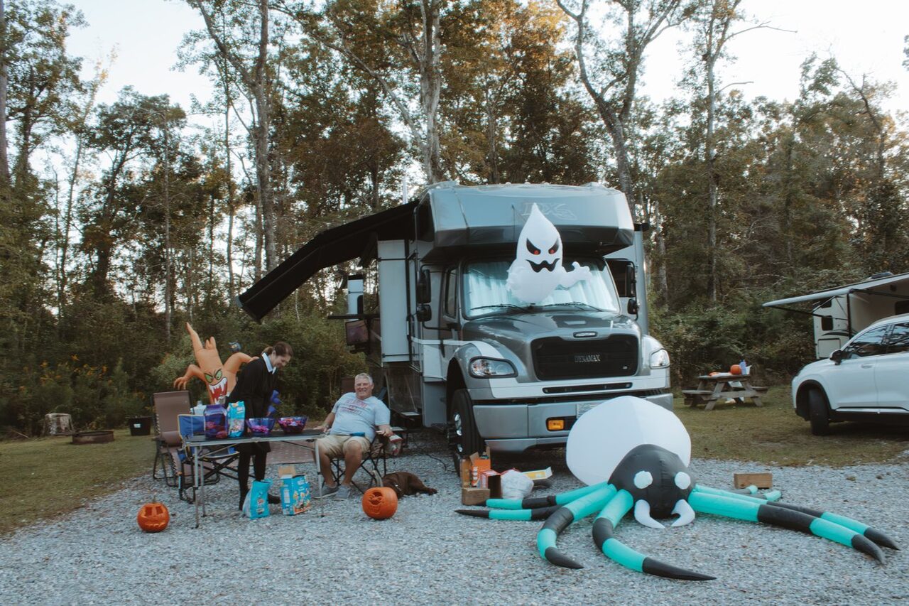 Two guests seated beside a decorated motorhome on a level gravel RV site at Fireside RV Resort