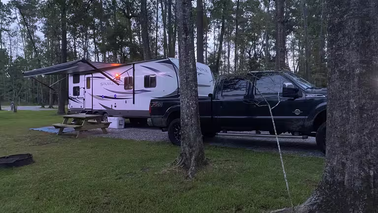 An RV set up with its awning out on a shaded site at Fireside RV Resort near New Orleans