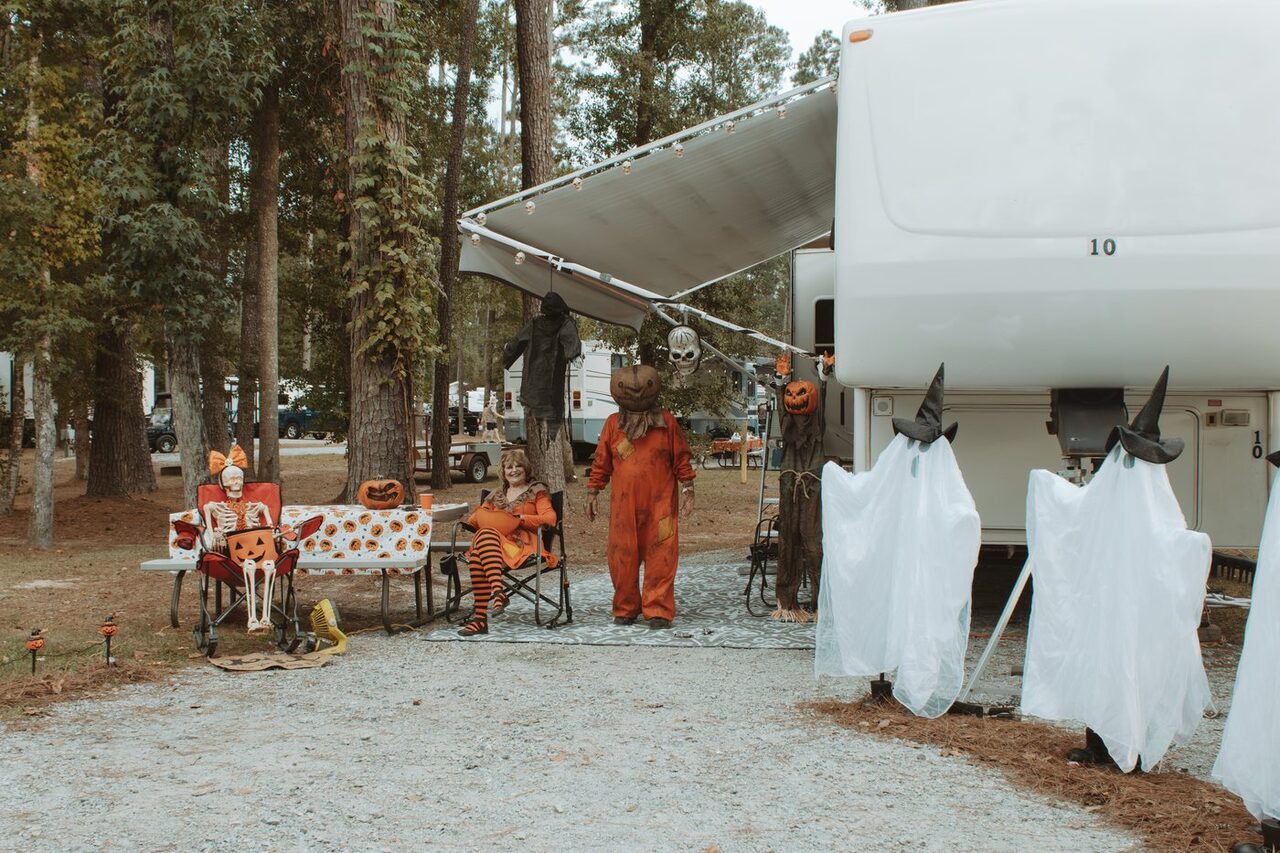 Guests in Halloween costumes beside a decorated fifth wheel RV under tall pines at Fireside RV Resort