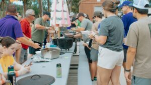 Guests serving themselves from cast iron pots at long tables during a holiday cookout while camping near New Orleans