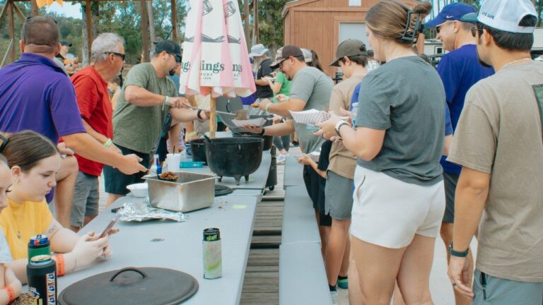 Guests serving themselves from cast iron pots at long tables during a holiday cookout while camping near New Orleans