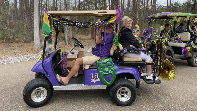 Man and woman riding a purple golf cart decorated with Mardi Gras beads, flags and a green mask at Fireside RV Resort near New Orleans