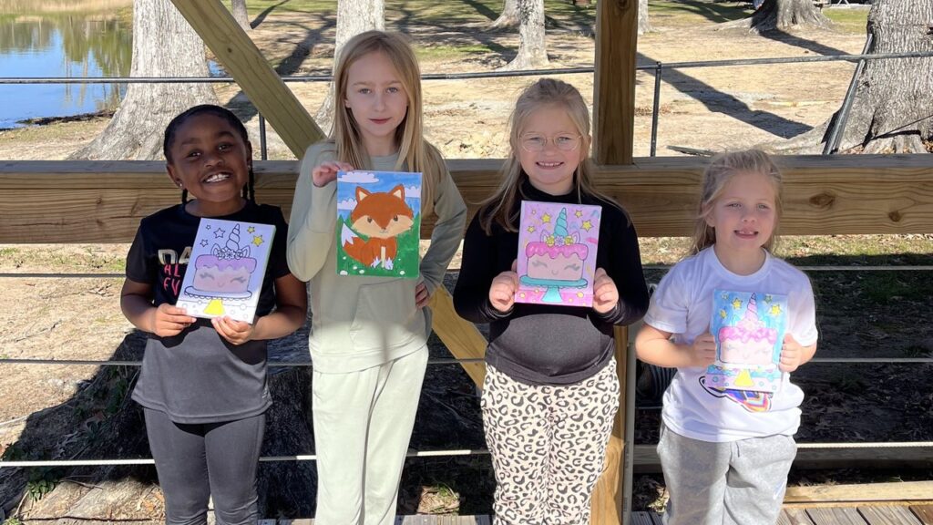 Four kids holding up their painted canvases under the lakeside pavilion at Fireside RV Resort in Ponchatoula, Louisiana