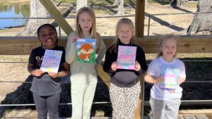 Four kids holding up their painted canvases under the lakeside pavilion at Fireside RV Resort in Ponchatoula, Louisiana
