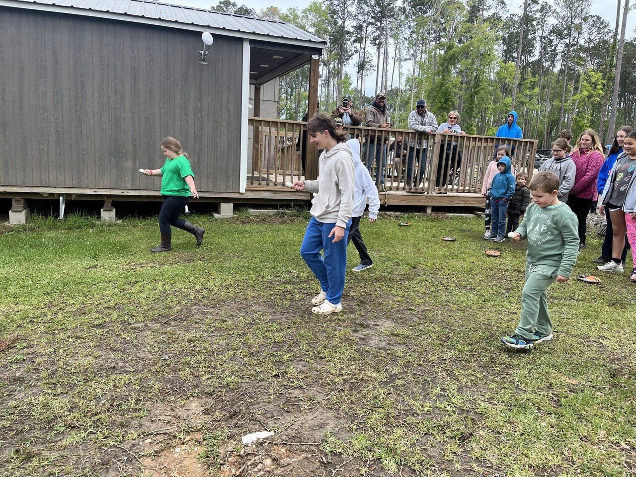 Kids running an egg-and-spoon race on the lawn as guests watch from a porch at Fireside RV Resort in Ponchatoula