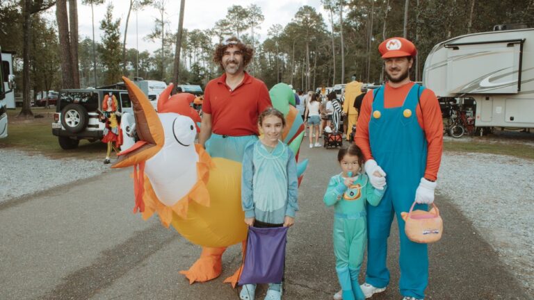 Family in Halloween costumes holding candy bags on a pine-lined road with RVs at Fireside RV Resort near Ponchatoula, Louisiana