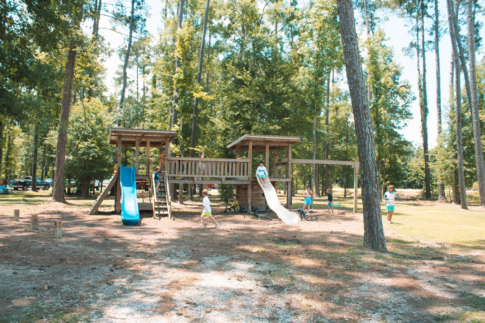 Kids play on a wooden playground with blue and white slides at Fireside RV Resort in Ponchatoula, Louisiana