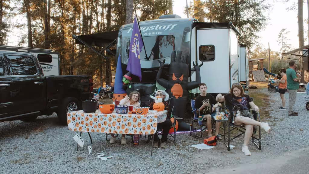 Family relaxing beside a Halloween-decorated table at their full hookup RV site under tall pines in Ponchatoula, Louisiana