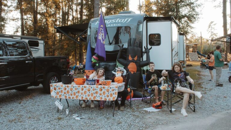 Family relaxing beside a Halloween-decorated table at their full hookup RV site under tall pines in Ponchatoula, Louisiana