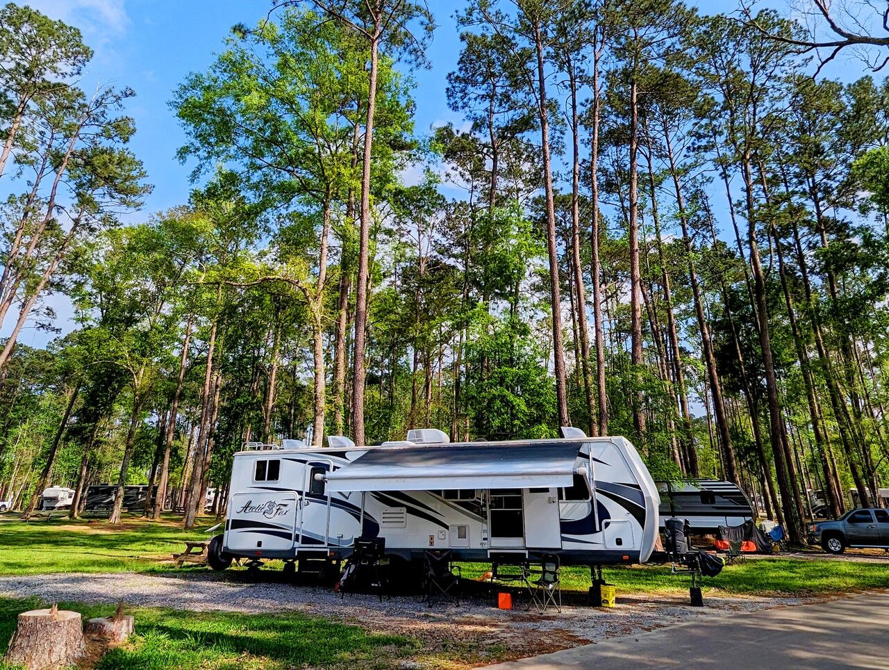 Travel trailer with its awning out on a full hookup RV site under tall pines at Fireside RV Resort in Ponchatoula, Louisiana