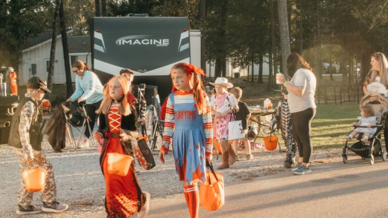 Kids in Halloween costumes trick-or-treating past a white glamping cabin and parked RVs at Fireside RV Resort in Ponchatoula, Louisiana