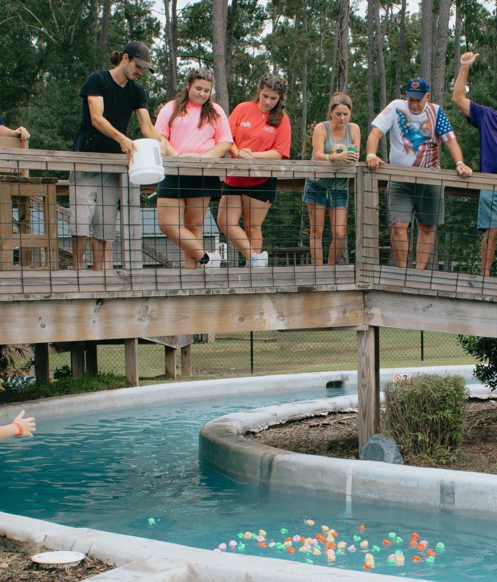 Guests lean on a wooden railing above the lazy river at Fireside RV Resort in Louisiana while small colorful toys float in the water below