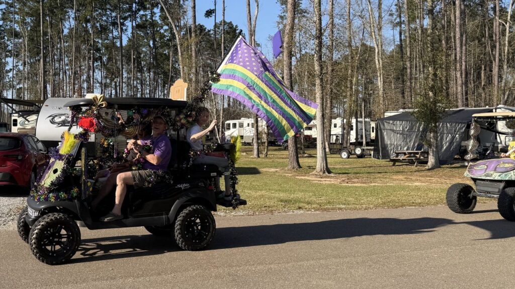A golf cart decorated for Mardi Gras with a purple, green and gold flag rolls past RV sites at Fireside RV Resort in Ponchatoula, Louisiana