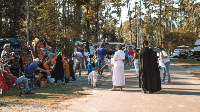 Costumed guests walk a leashed white dog down a pine-shaded loop at Fireside RV Resort, a pet friendly RV park in Ponchatoula, Louisiana