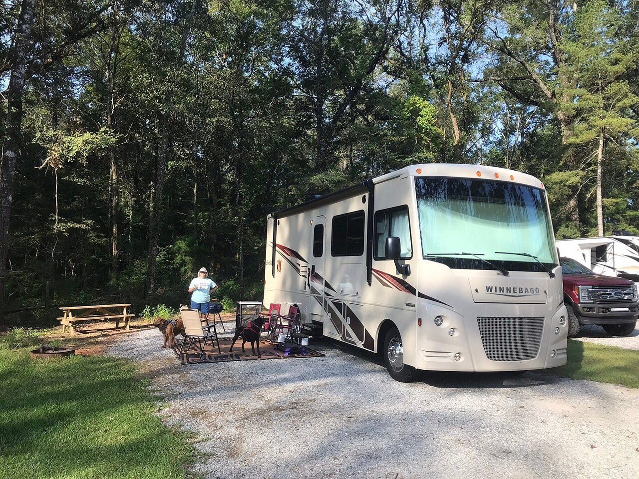Two dogs on an outdoor rug beside a motorhome at a shaded pet friendly RV site at Fireside RV Resort in Louisiana