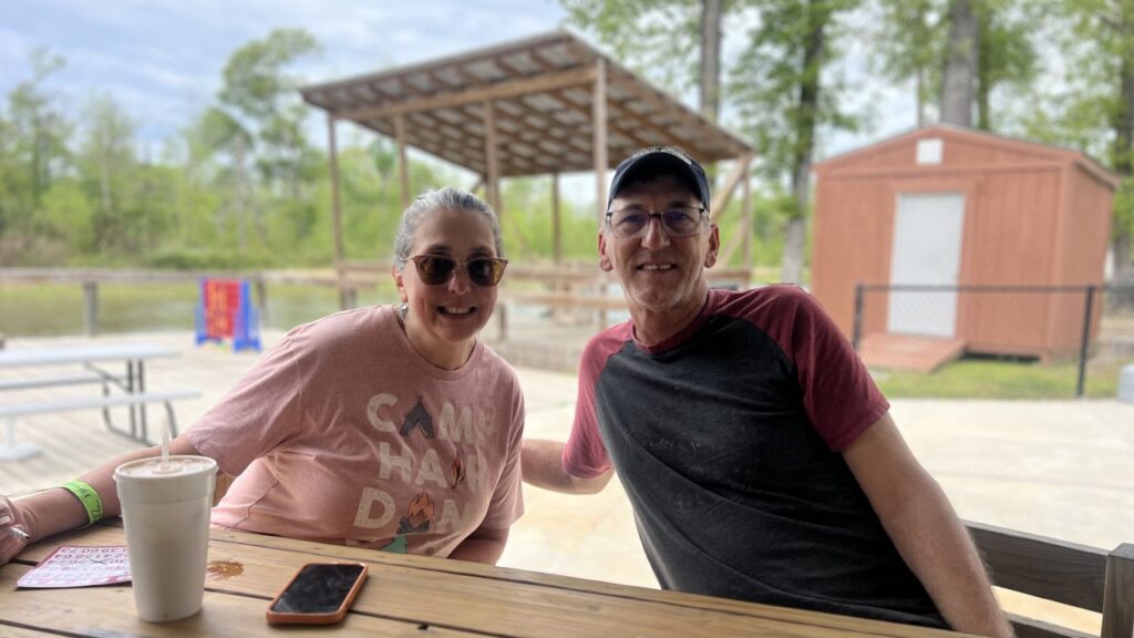 Two smiling guests at a picnic table by the pond at Fireside RV Resort in Ponchatoula, Louisiana