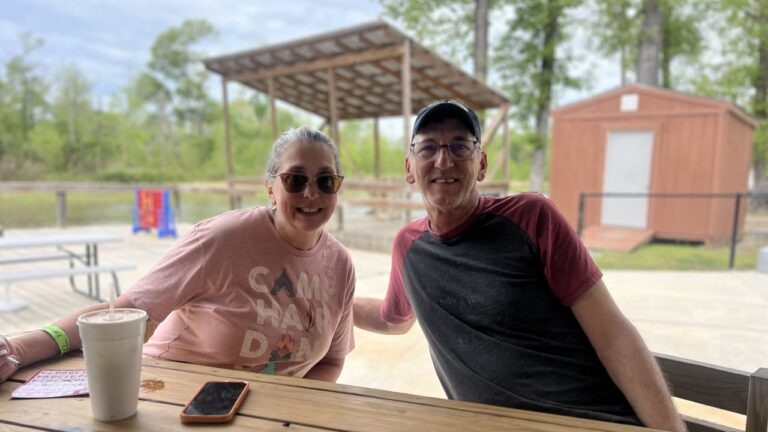 Two smiling guests at a picnic table by the pond at Fireside RV Resort in Ponchatoula, Louisiana