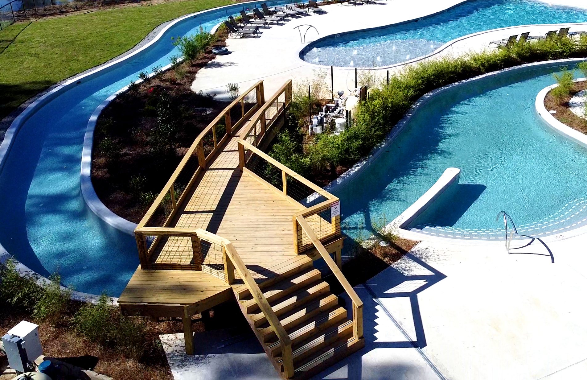 Aerial view of the lazy river, a wooden footbridge and the swimming pool at Fireside RV Resort, an RV park with a swimming pool near New Orleans