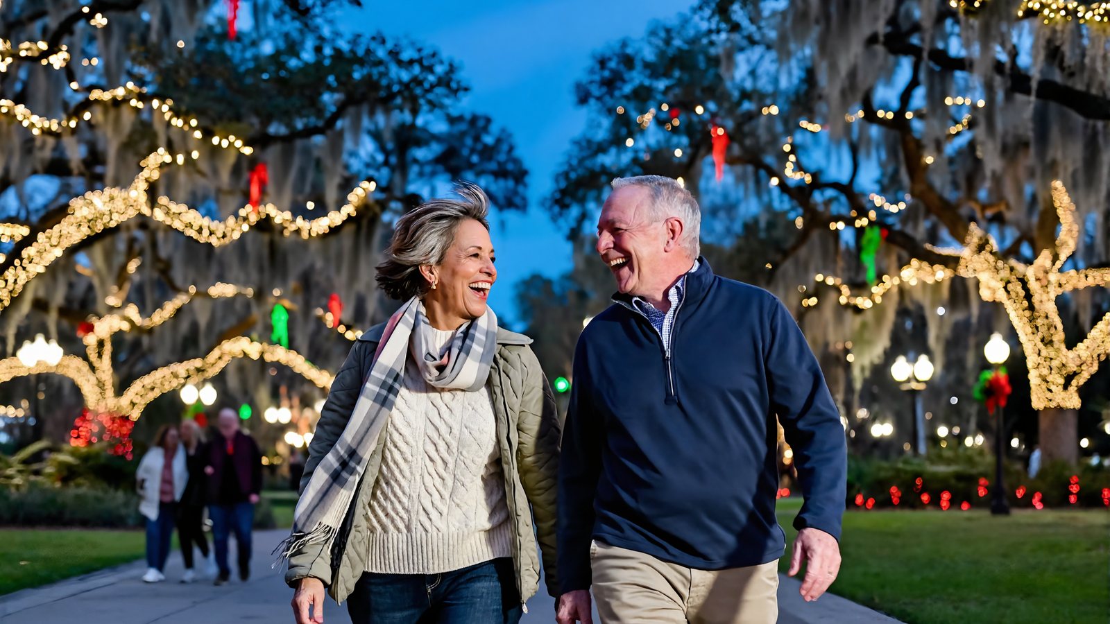 A man and a woman laugh while strolling under moss-draped live oaks wrapped in holiday lights on a South Louisiana winter evening
